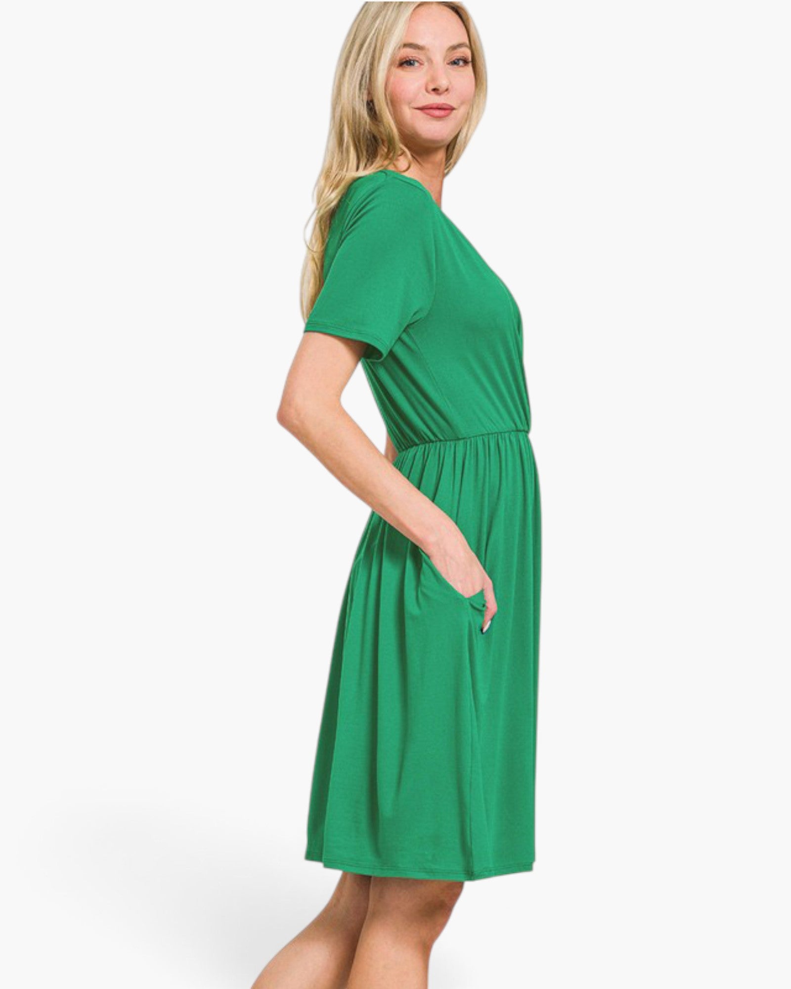 A woman modeling a bright green short-sleeve dress with a gathered waist and side pockets, photographed against a clean white studio background.