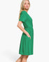 A woman modeling a bright green short-sleeve dress with a gathered waist and side pockets, photographed against a clean white studio background.