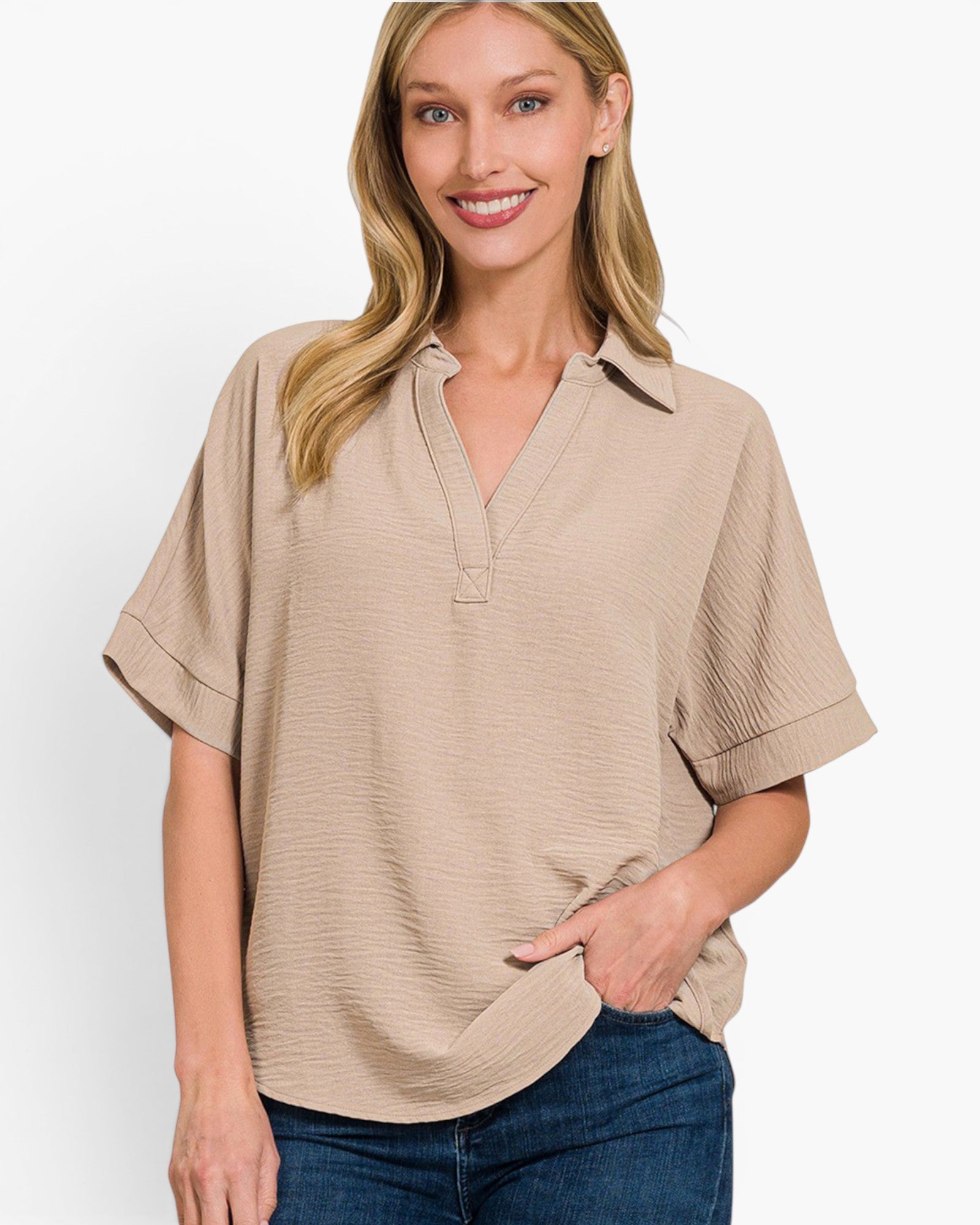 A woman wearing a beige short-sleeve collared top with a relaxed fit and blue jeans, photographed against a clean white studio background.