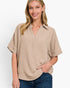 A woman wearing a beige short-sleeve collared top with a relaxed fit and blue jeans, photographed against a clean white studio background.
