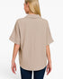 A woman shown from the back wearing a light beige short-sleeve collared blouse with a textured crinkle fabric, paired with dark blue jeans, against a plain white background.