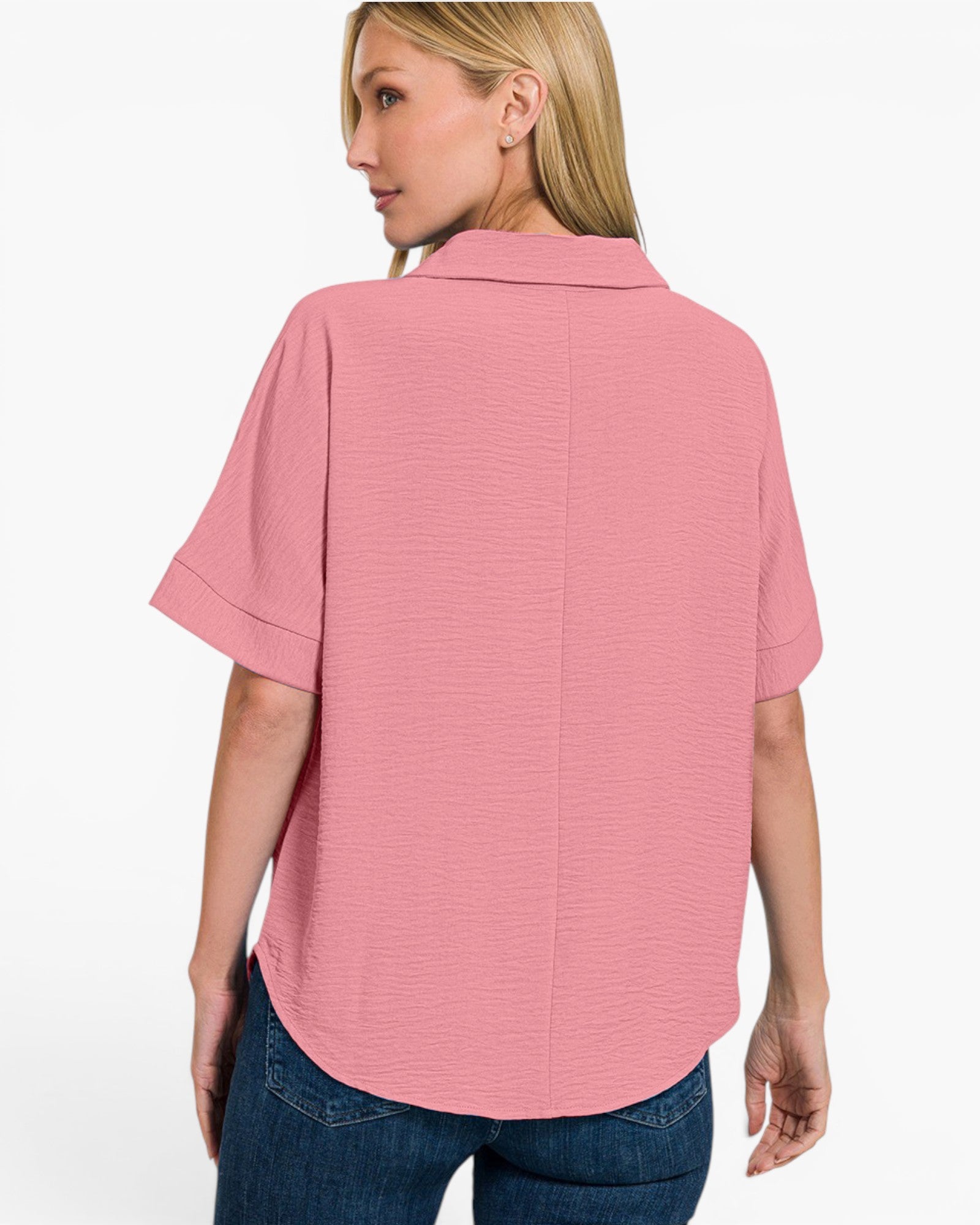 A woman shown from the back wearing a short-sleeve pink collared top with a subtle textured horizontal stripe pattern, paired with blue jeans, against a plain white studio background.
