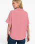 A woman shown from the back wearing a short-sleeve pink collared top with a subtle textured horizontal stripe pattern, paired with blue jeans, against a plain white studio background.