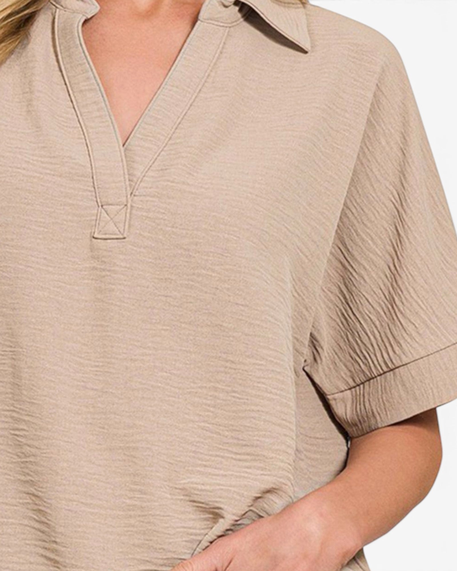 Close-up of a beige crinkled short-sleeve top with a split V-neck and rolled cuffs, worn by a model.