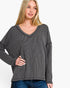 A woman wearing a dark gray ribbed knit long-sleeve sweater with a V-neck, paired with blue jeans, against a plain white background.
