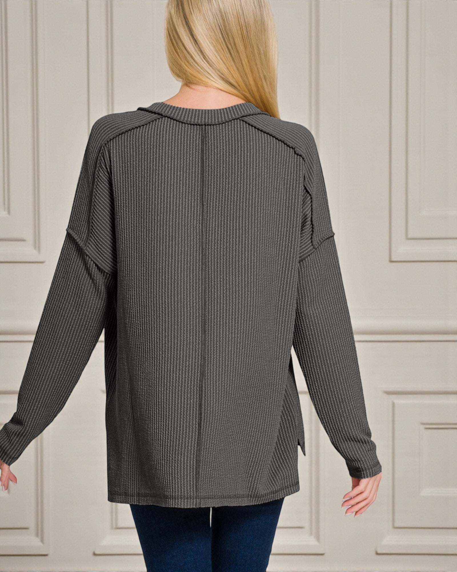 Person wearing a gray ribbed sweater against a neutral wall