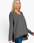 A woman wearing a dark gray ribbed knit long-sleeve top with a V-neck and high-low hem, paired with blue jeans, against a plain white background.