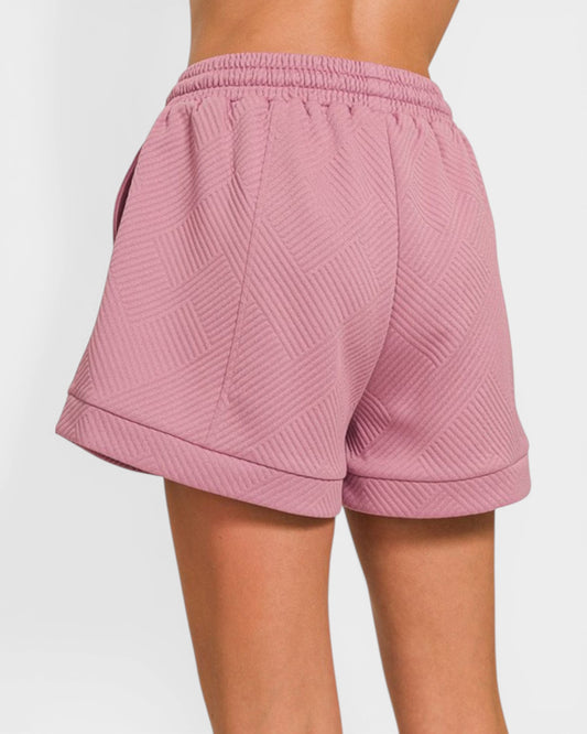 Pink shorts with a textured pattern worn by a person on a white background