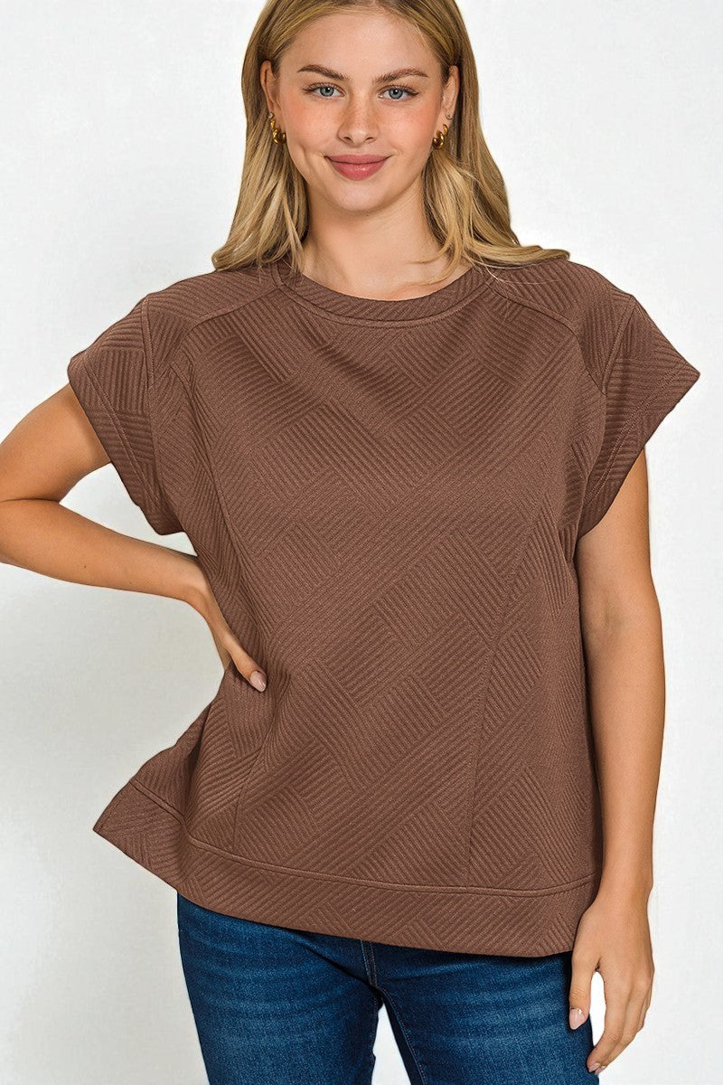 Woman wearing a brown textured top and blue jeans on a white background