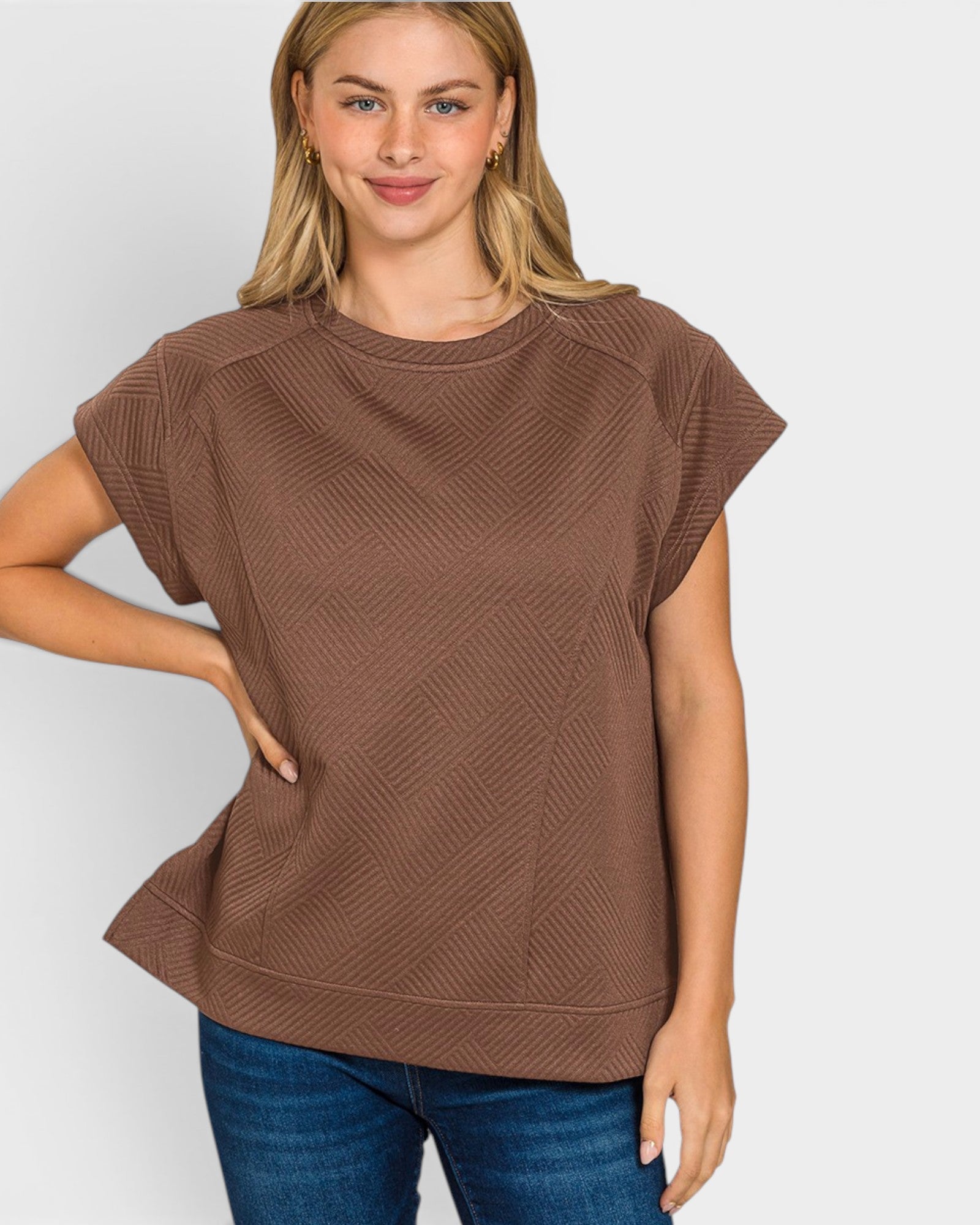 Woman wearing a brown textured top and blue jeans on a white background
