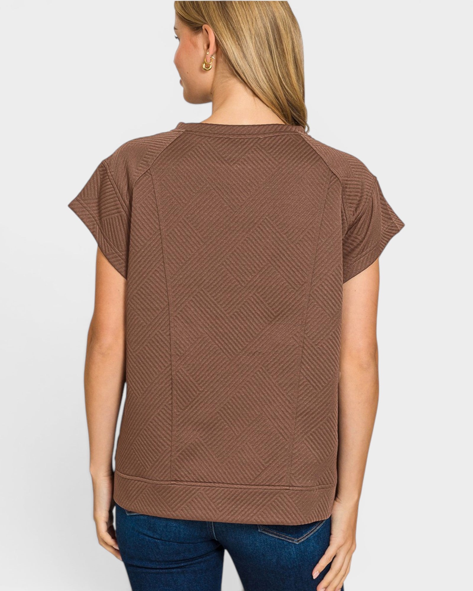 Woman wearing a brown textured top and blue jeans on a white background