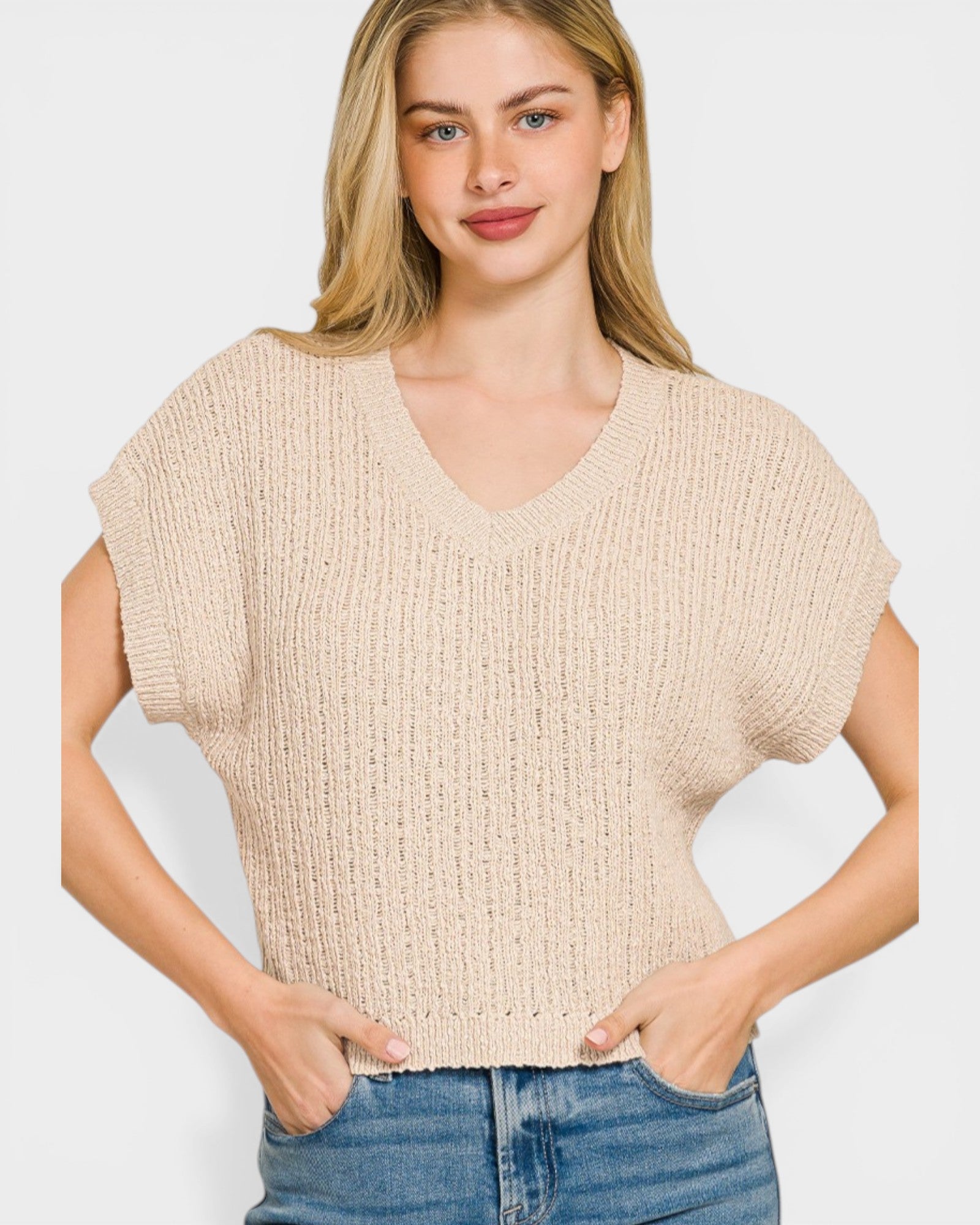 Woman wearing a beige sleeveless knitted top against a white background
