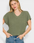 Woman wearing a green ribbed sweater and blue jeans against a white background