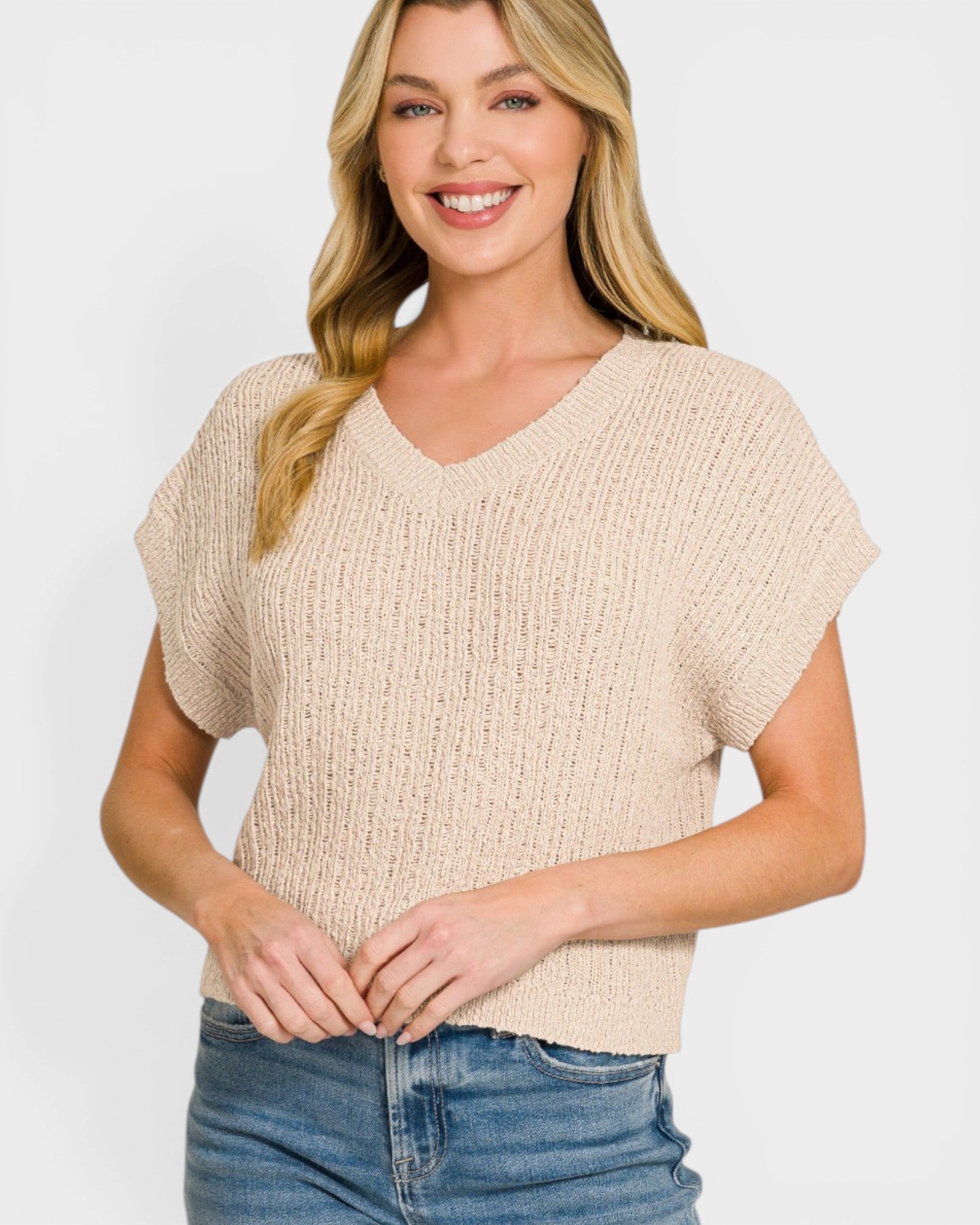 Woman wearing a beige knitted top and blue jeans on a white background