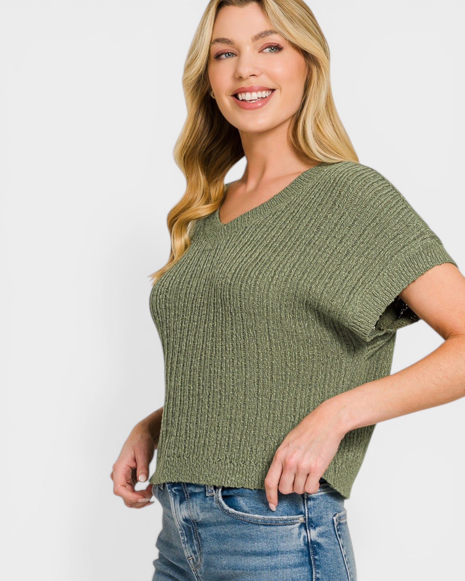 Woman wearing a green ribbed sweater and blue jeans on a white background