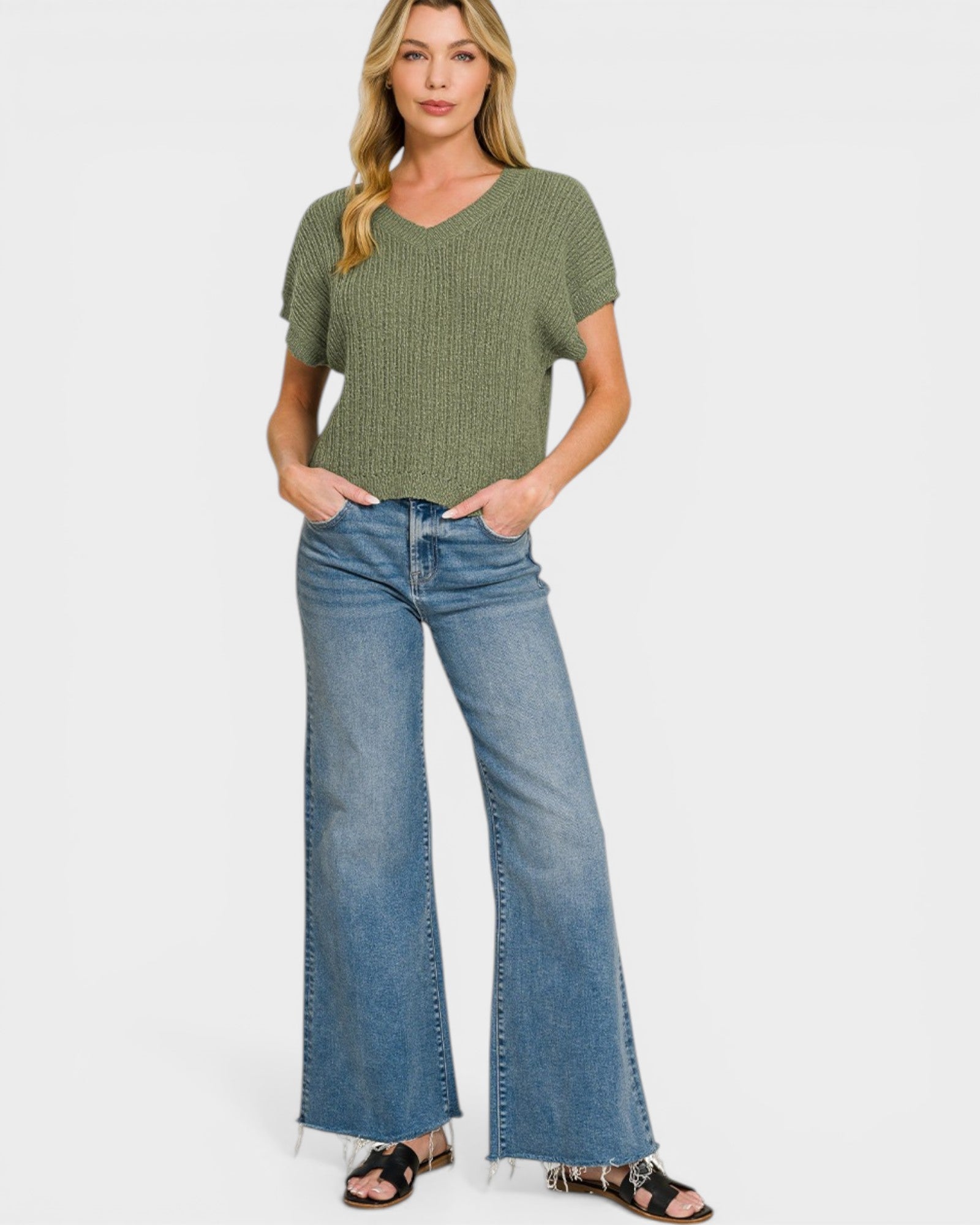 Woman wearing a green patterned top and blue jeans on a white background