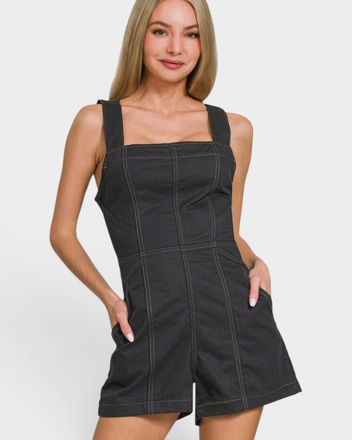 Woman wearing a black denim overall dress against a white background