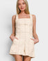 Woman wearing a beige pinafore dress against a plain background