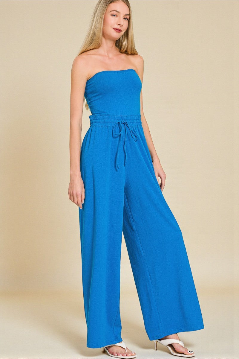 Woman wearing a blue strapless jumpsuit on a beige background