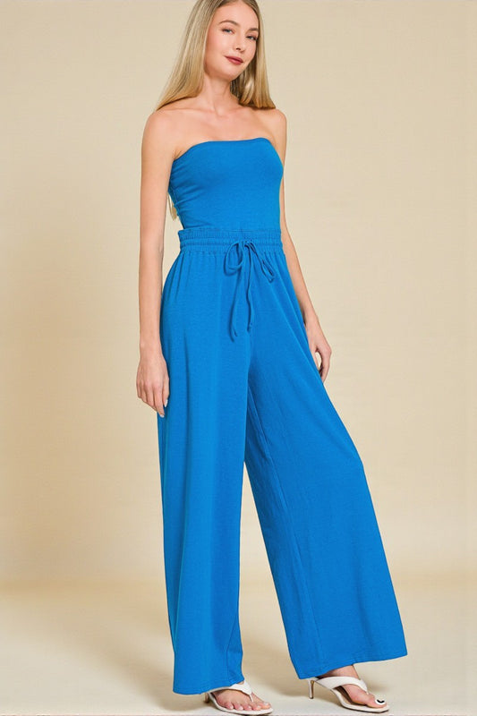 Woman wearing a blue strapless jumpsuit on a beige background