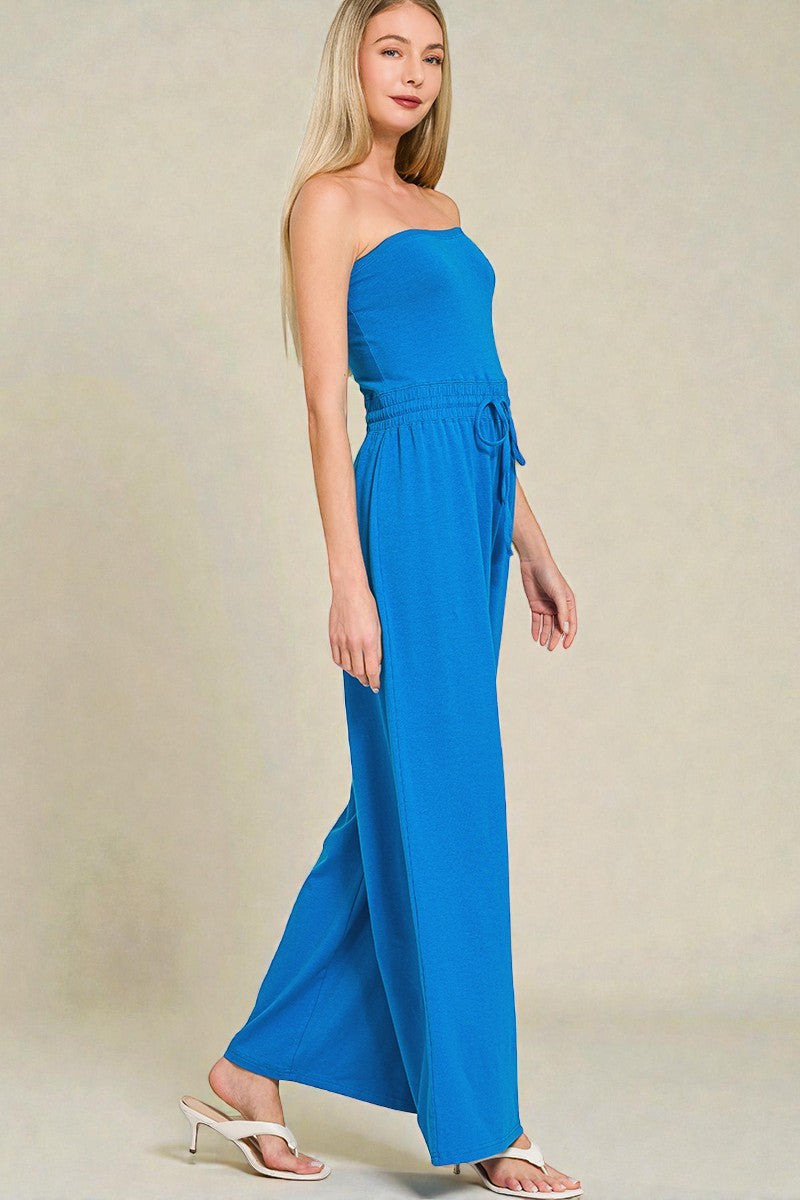 Woman wearing a blue strapless jumpsuit on a beige background