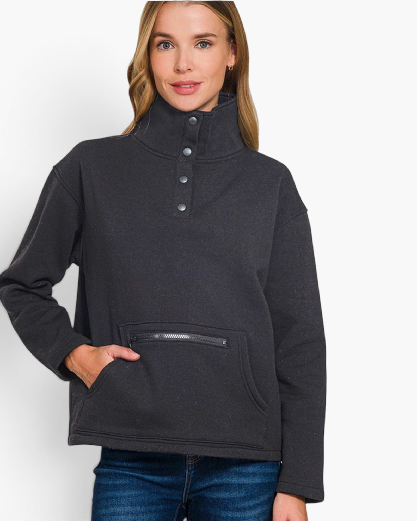 A woman wearing a dark charcoal gray mock neck pullover sweater with a buttoned placket and a zippered front pocket, paired with blue jeans, against a plain white background.