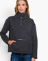 A woman wearing a dark charcoal gray mock neck pullover sweater with a buttoned placket and a zippered front pocket, paired with blue jeans, against a plain white background.