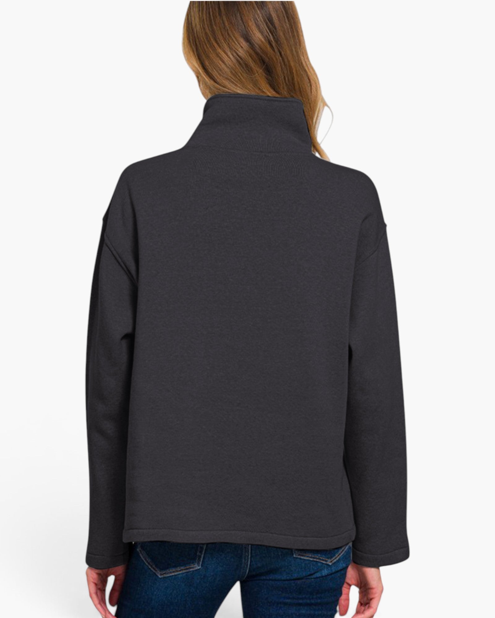 A woman viewed from the back wearing a dark charcoal gray mock neck fleece jacket and blue jeans, set against a plain white studio background.