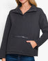 A woman wearing a dark charcoal gray long-sleeve pullover sweater with a half-placket snap collar, a zippered front pocket, and a hand in her pocket, paired with blue jeans against a plain white background.