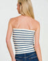Woman wearing a strapless navy and white striped top with blue jeans on a plain background