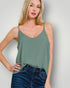 Woman wearing a green tank top and blue jeans against a plain background