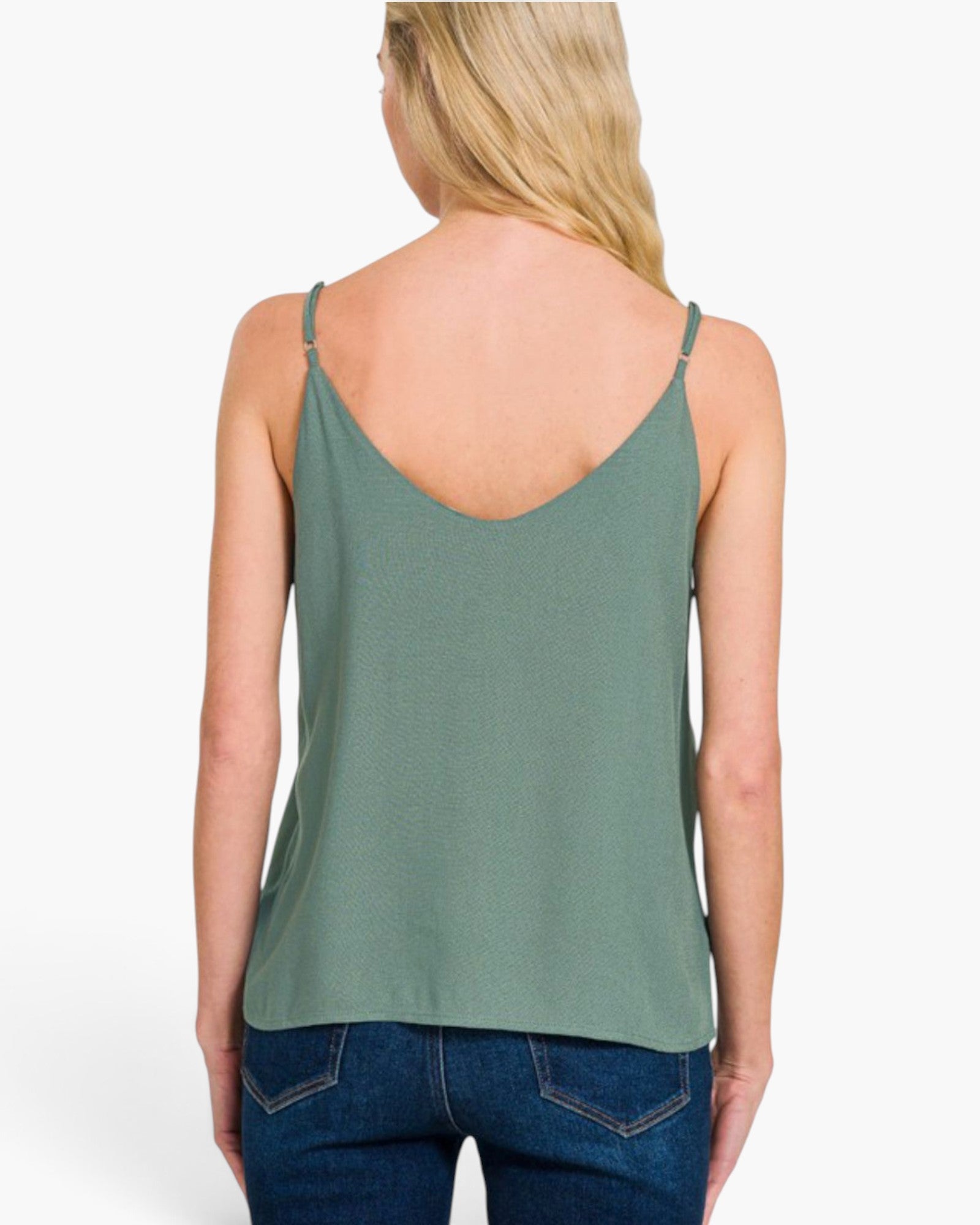 A woman shown from the back wearing a sage green spaghetti-strap tank top and blue jeans against a plain white studio background.