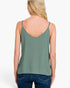 A woman shown from the back wearing a sage green spaghetti-strap tank top and blue jeans against a plain white studio background.