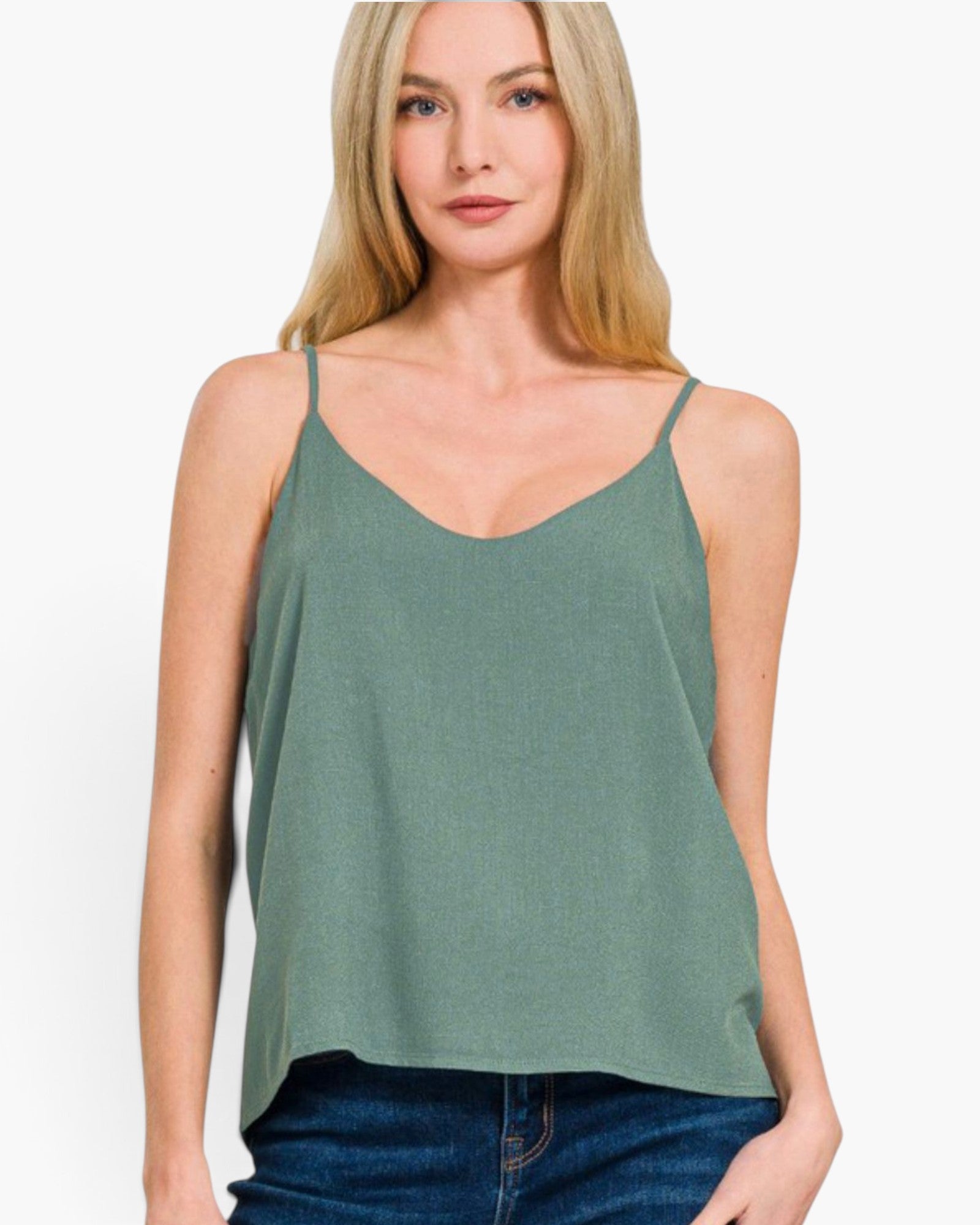 A woman wearing a sage green spaghetti-strap camisole top and blue jeans, photographed against a clean white studio background.