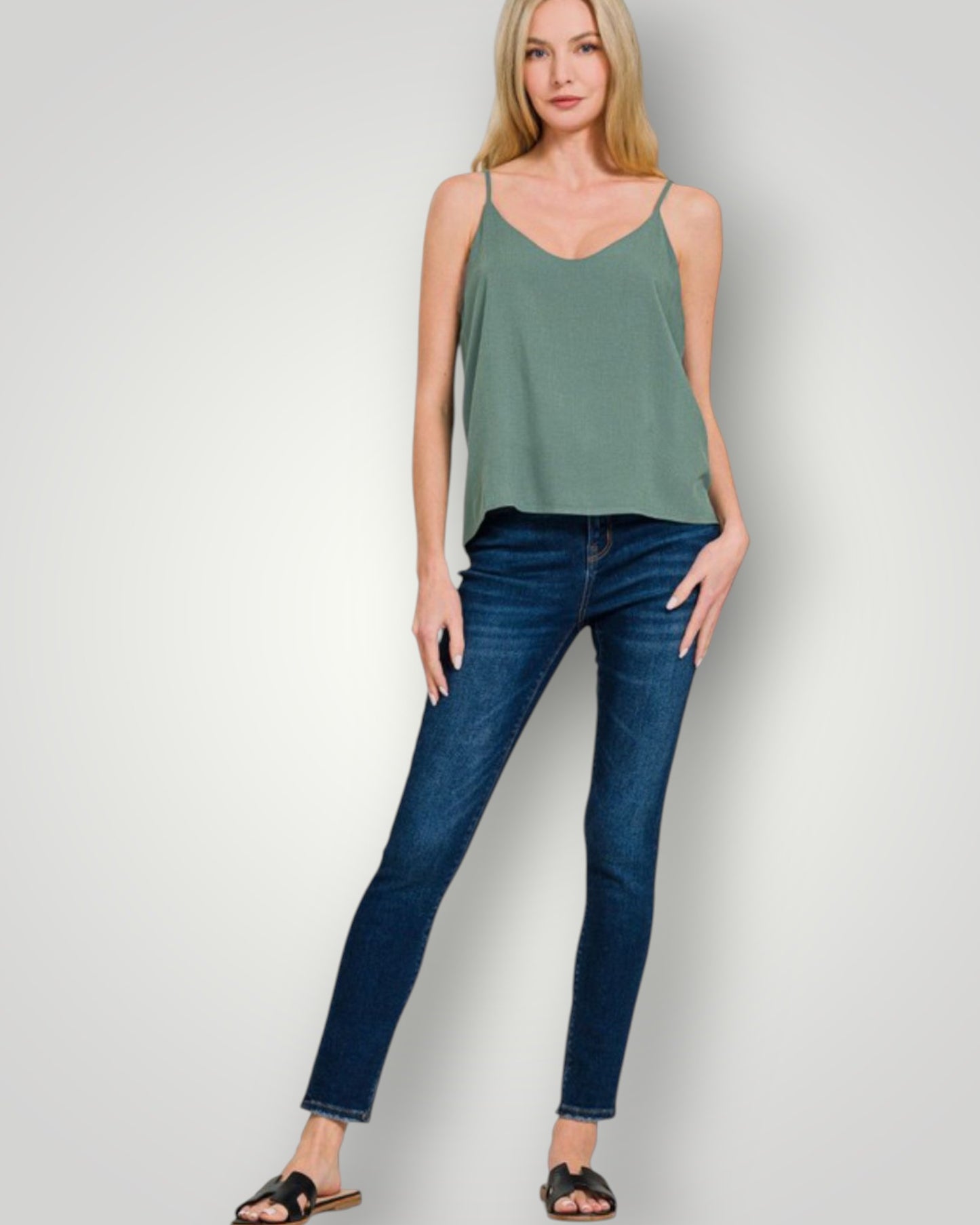 Woman wearing a green tank top and blue jeans on a white background