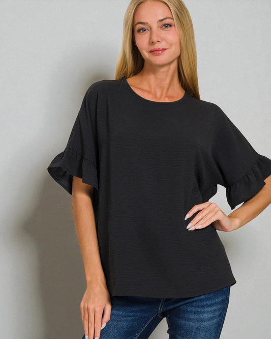 Woman wearing a black blouse with ruffled sleeves against a plain background