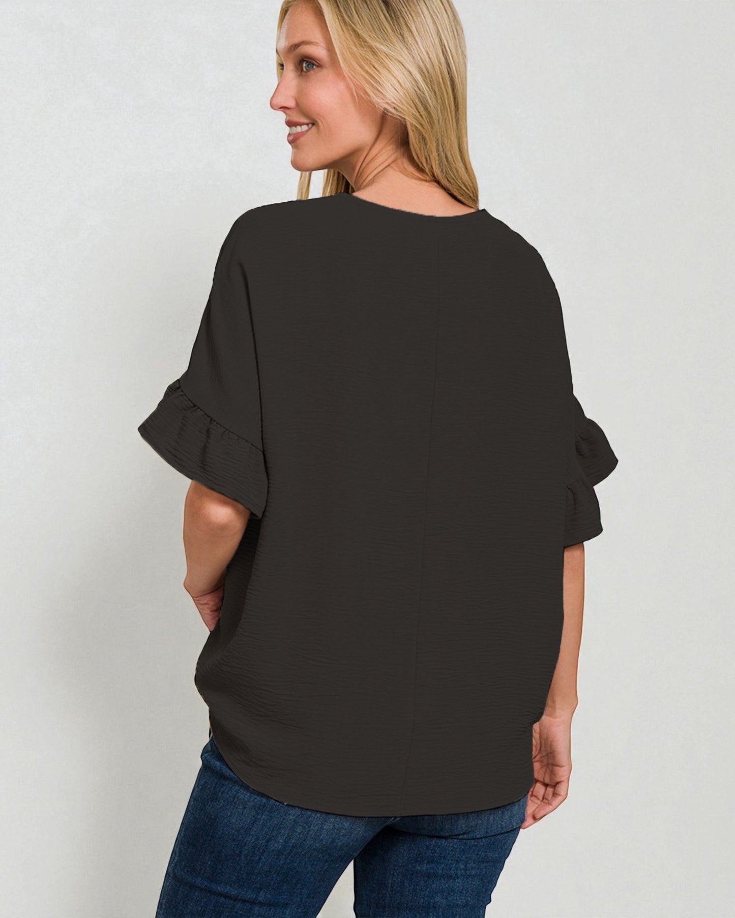 Woman wearing a black blouse with ruffled sleeves on a plain background