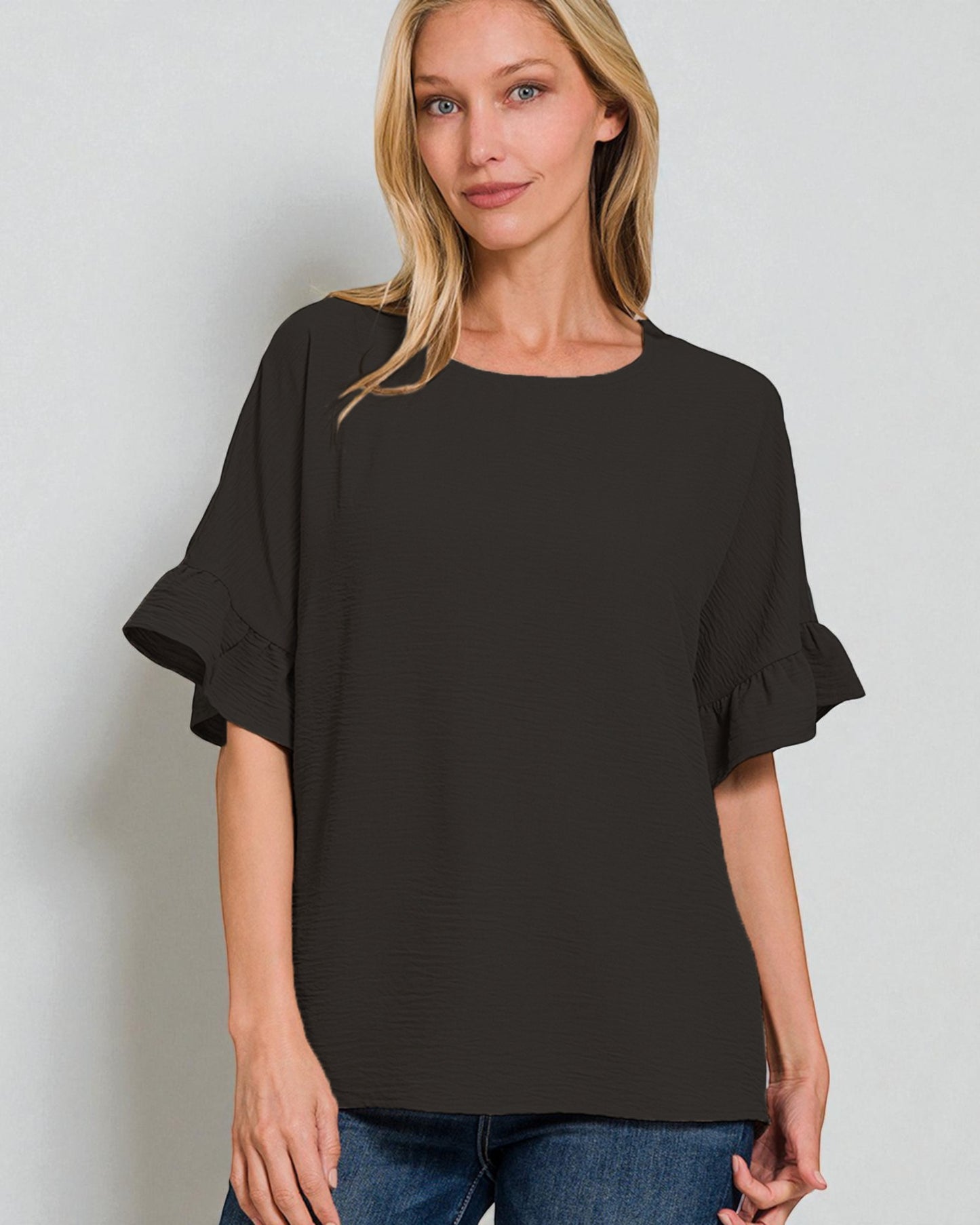 Woman wearing a black blouse with ruffled sleeves against a plain background