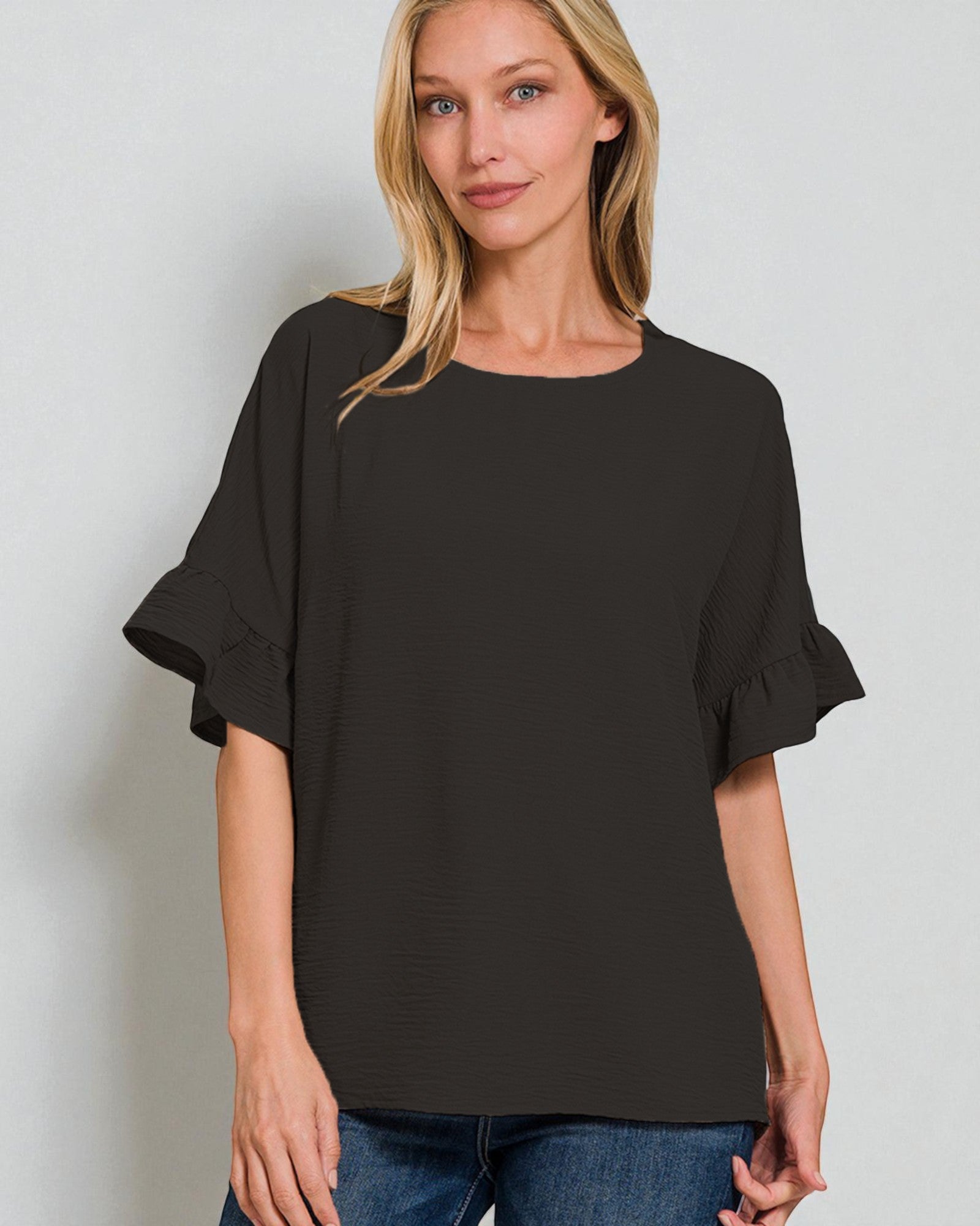 Woman wearing a black blouse with ruffled sleeves against a plain background