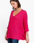 A woman wearing a bright pink ribbed knit top with a V-neck and elbow-length sleeves, paired with blue jeans, against a plain white background.