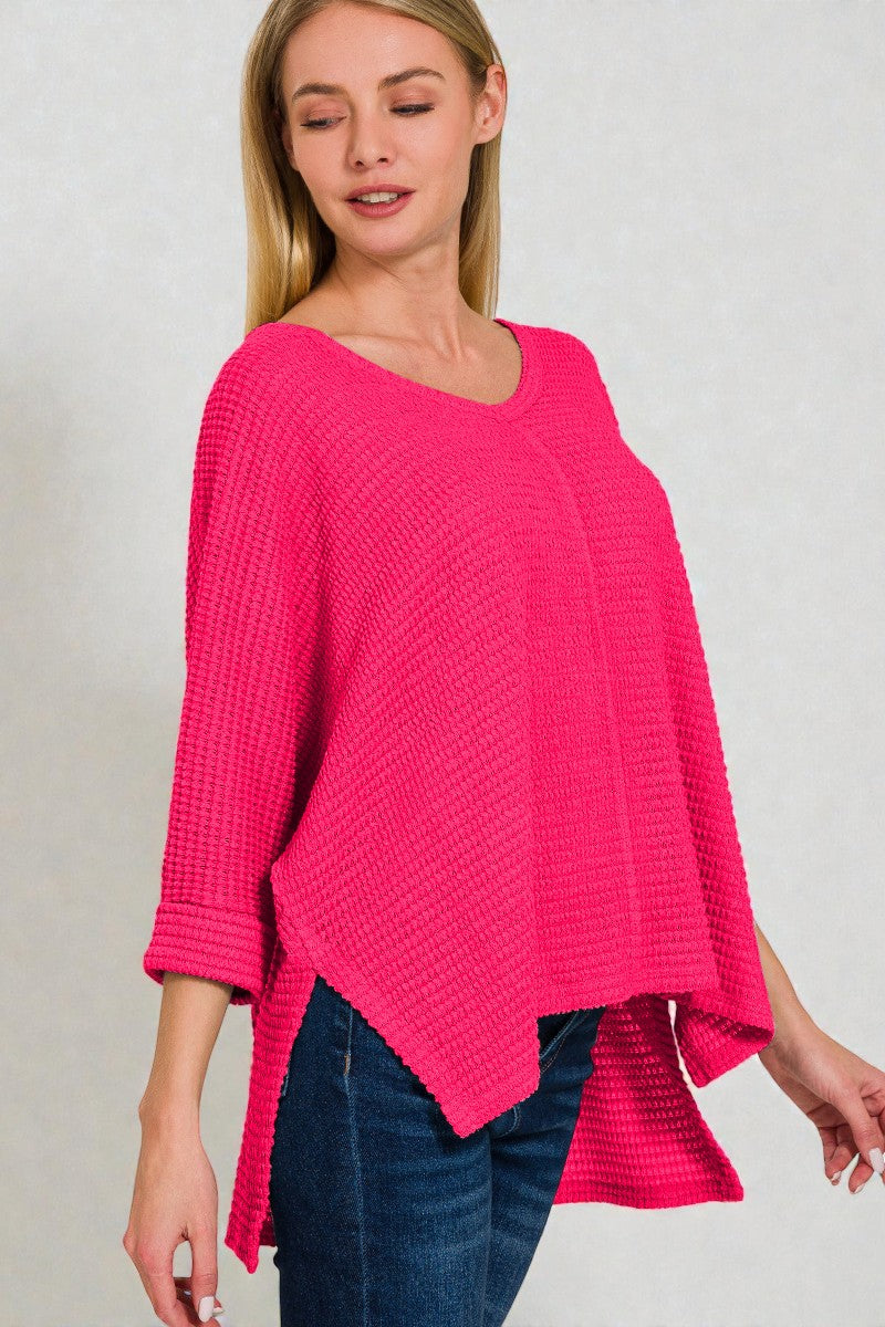 Woman wearing a bright pink knitted sweater with a plain background