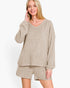 A woman modeling a matching beige lounge set consisting of a long-sleeve V-neck knit top and coordinating shorts, photographed against a clean white studio background.
