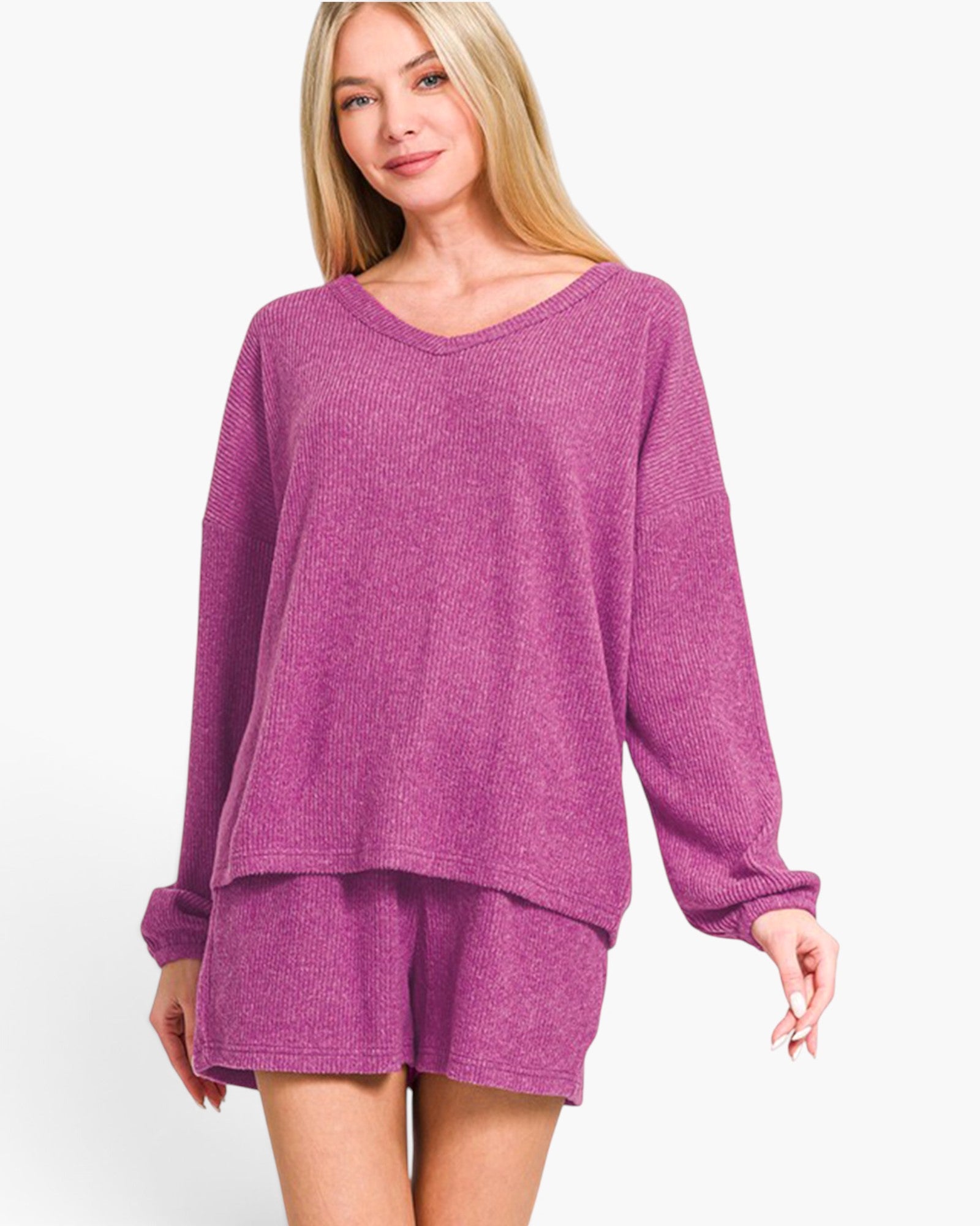 A woman modeling a matching knit loungewear set in heathered magenta-purple, featuring a long-sleeve V-neck top and coordinating shorts, against a plain white studio background.