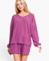 A woman modeling a matching knit loungewear set in heathered magenta-purple, featuring a long-sleeve V-neck top and coordinating shorts, against a plain white studio background.