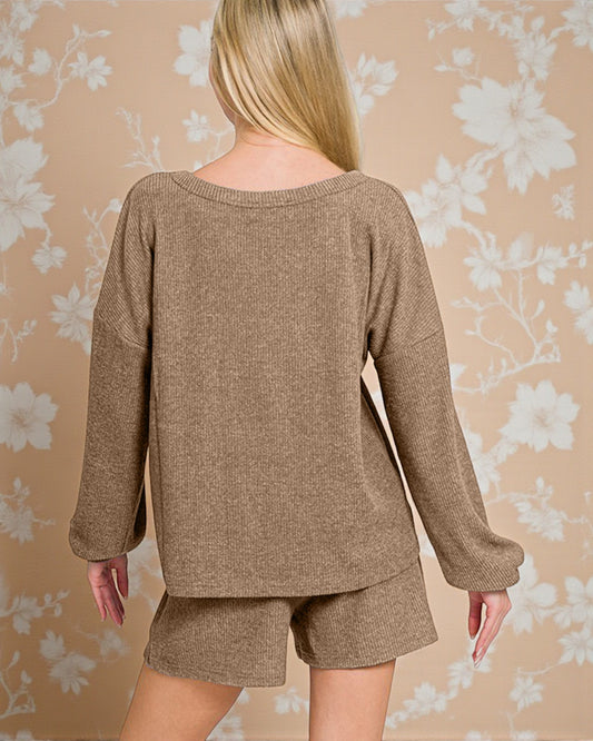 Person wearing a brown sweater and shorts set against a floral patterned wall.