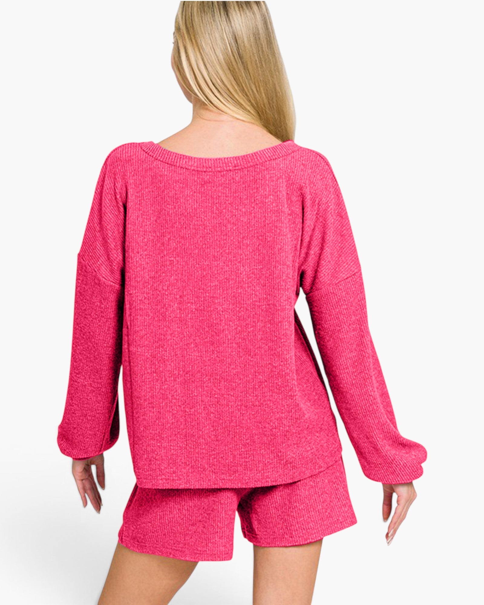 A woman shown from the back wearing a bright pink knit long-sleeve top and matching shorts against a plain light background.