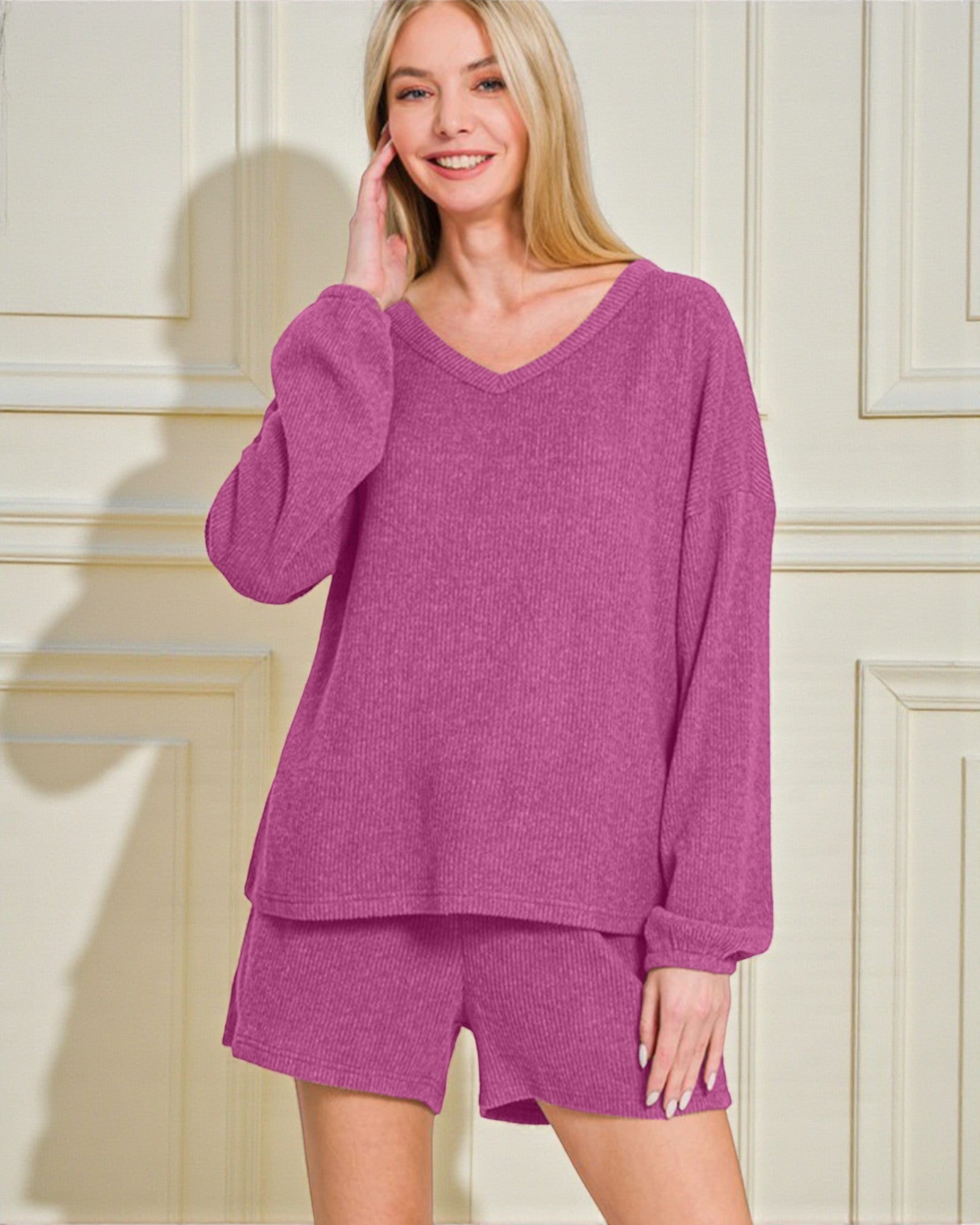 Woman wearing a pink lounge set against a white paneled wall.