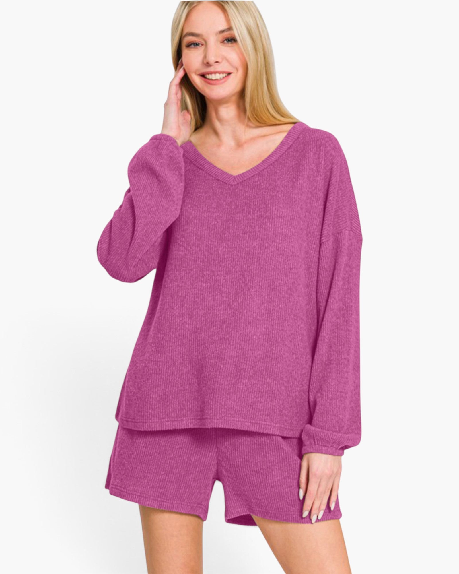 A woman modeling a matching two-piece loungewear set in a heathered magenta-purple color, featuring a long-sleeve V-neck top and coordinating shorts, against a plain white studio background.