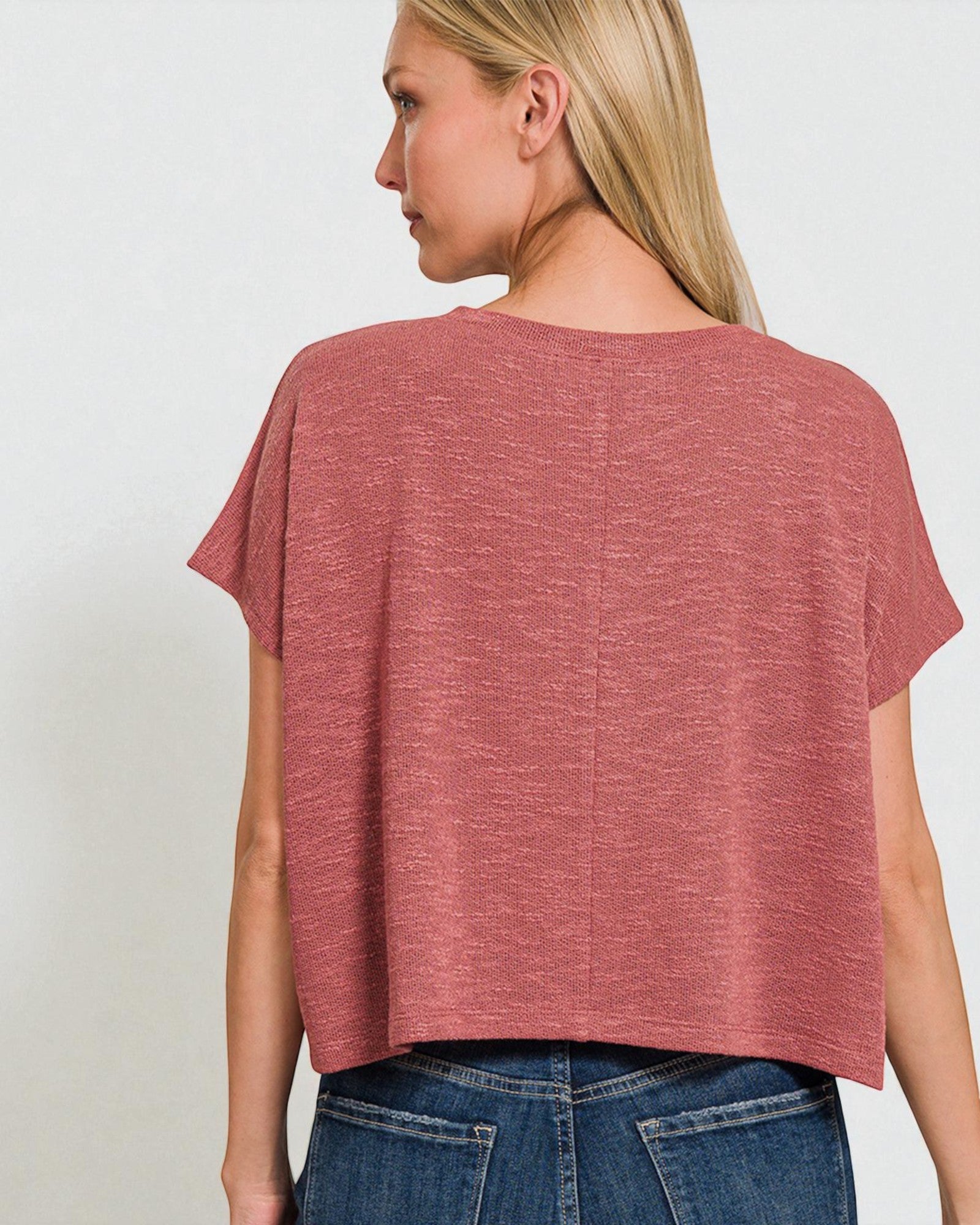 Woman wearing a loose-fitting, short-sleeve, rust-colored top against a plain background