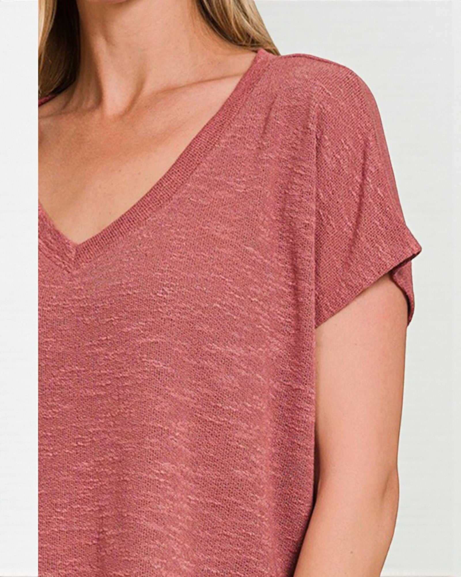 Close-up of a person wearing a pinkish-red short-sleeve top against a light gray background